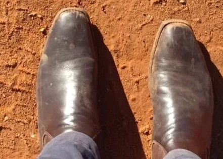 A person's feet in rustic shoes standing on red soil.